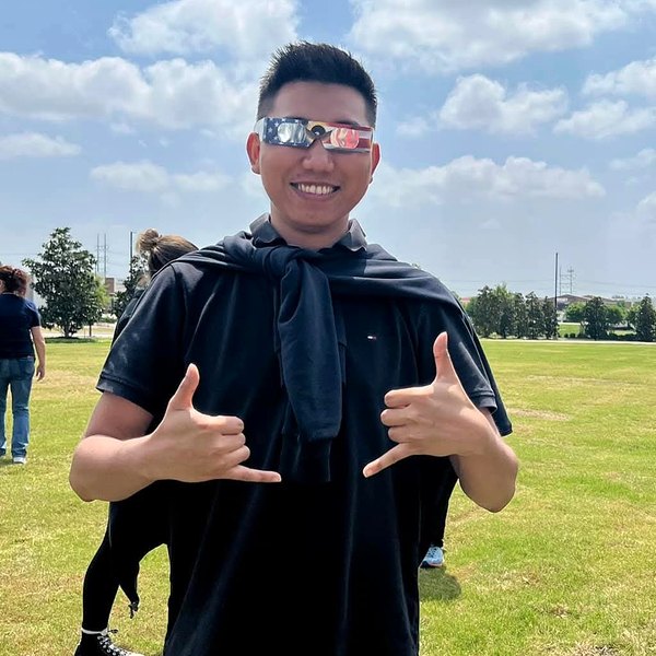 Min wearing eclipse glasses and making shaka signs in a park
